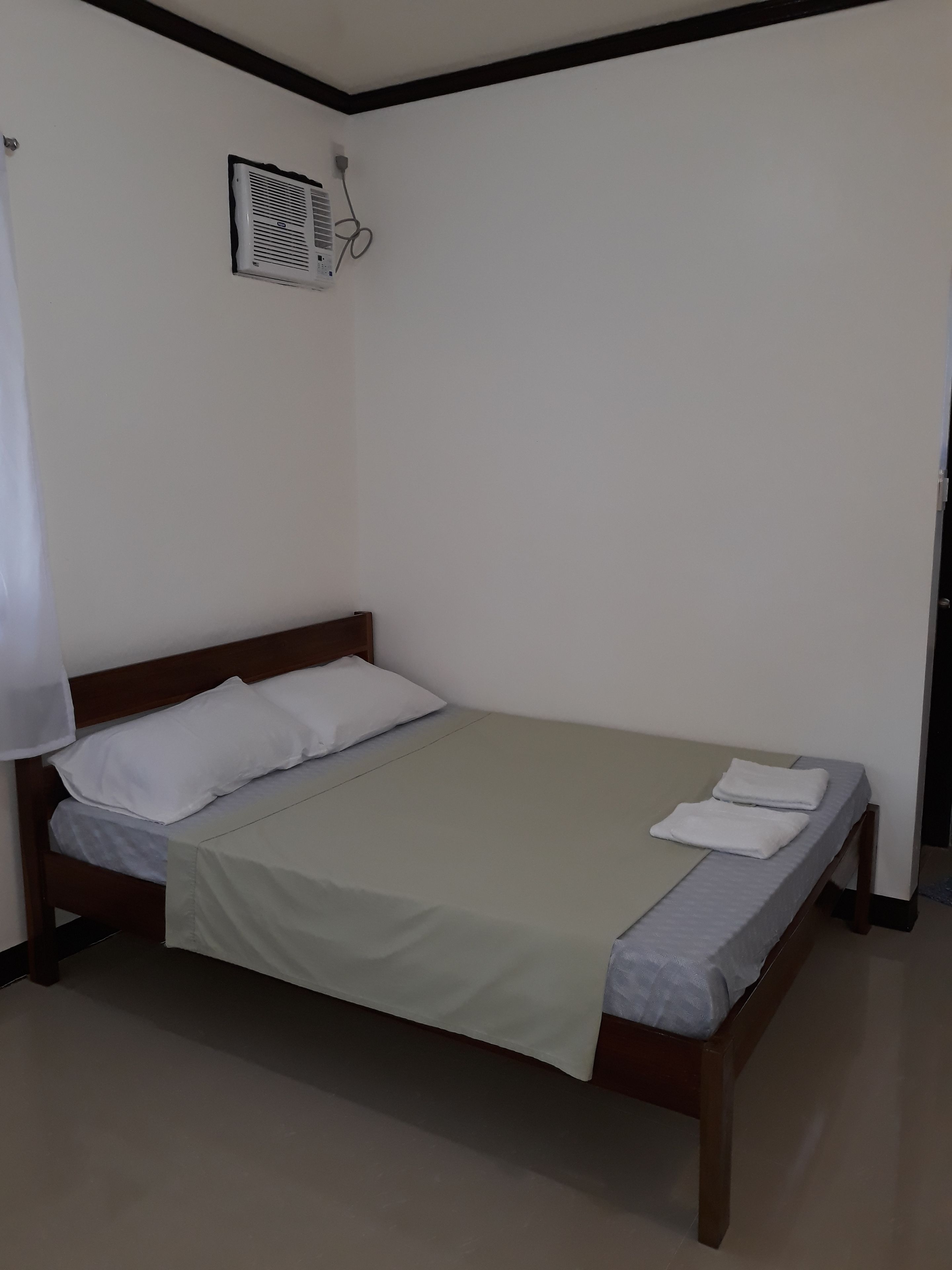 A single bed with a wooden frame, white bedding, and a beige blanket.