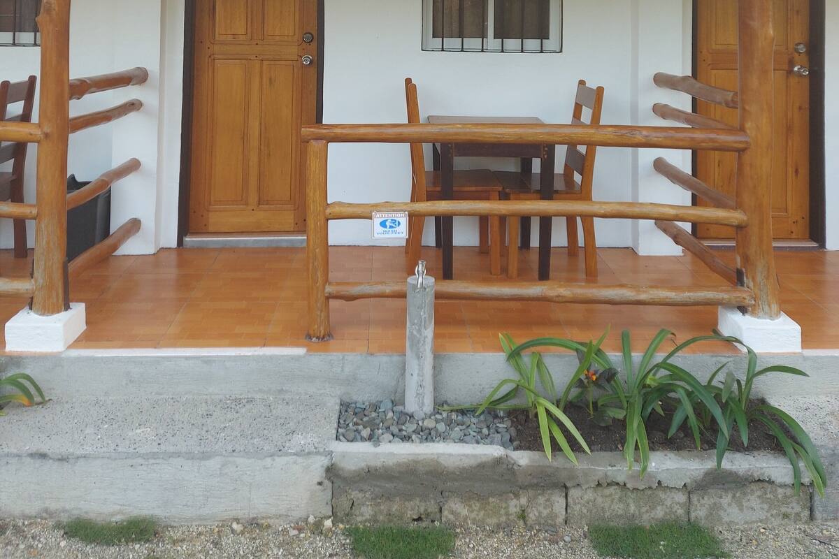 Un edificio con fachada blanca, techo de tejas y un porche de madera con un banco.