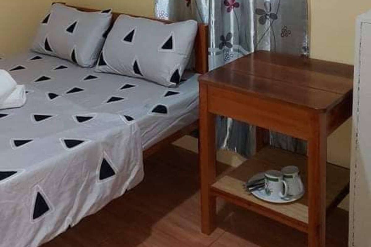 A small room with a bed, a table, and a window with curtains.