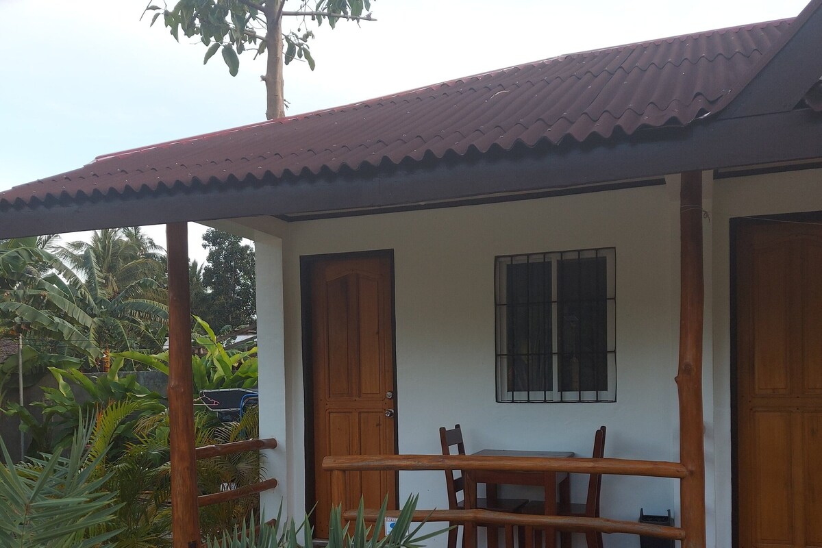 A house with a covered porch, a dining table, and chairs. There is a window with bars and a door with a wooden frame.