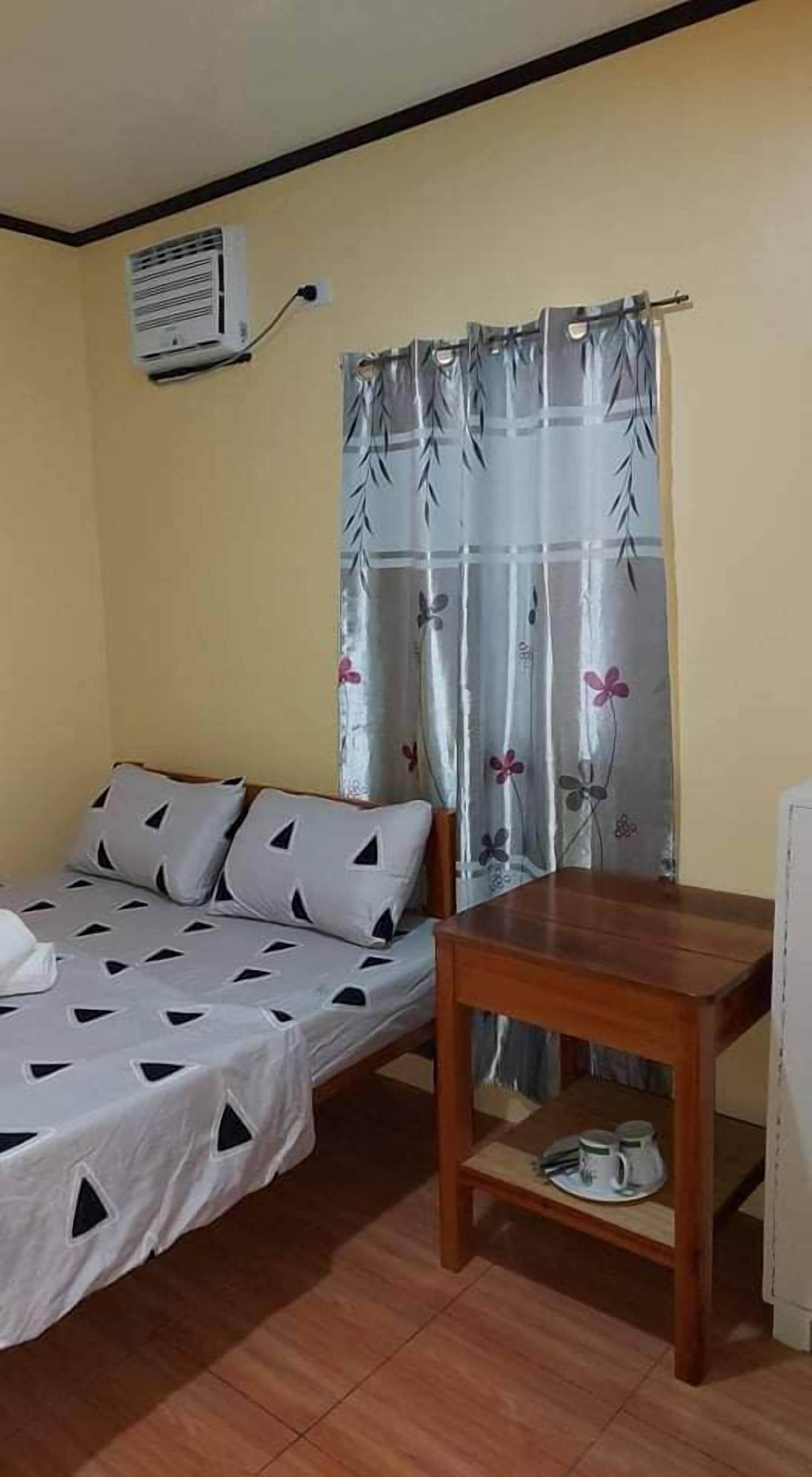 A small room with a bed, a table, and a window with curtains.