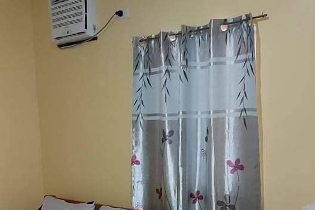 A small room with a bed, a table, and a window with curtains.