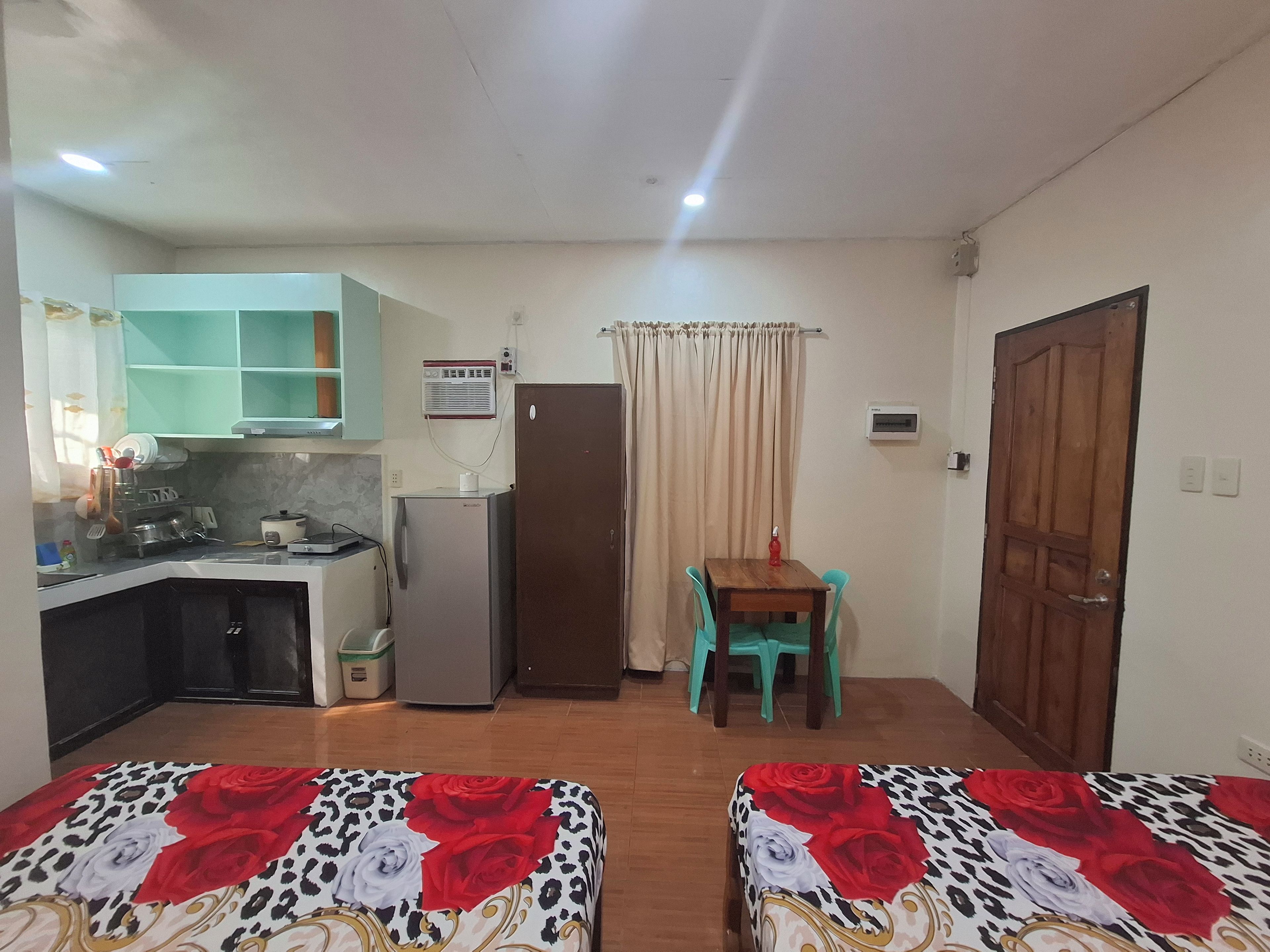 A compact room with a kitchenette, a single table with chairs, and two beds with floral bedding.