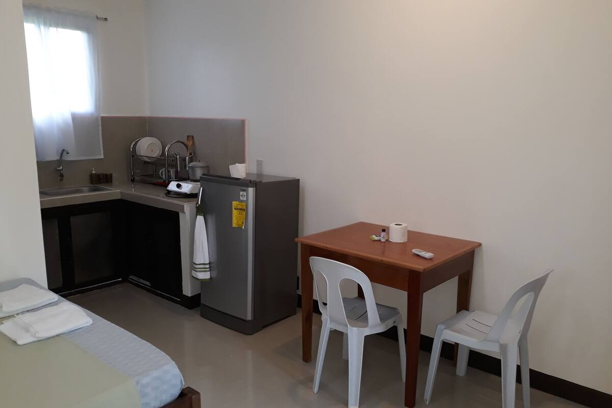 Cocina compacta con lavamanos, refrigerador y una pequeña mesa de comedor con dos sillas.