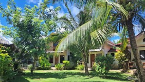 A tropical garden with palm trees, a thatched-roof building, and a well-maintained lawn. - Gardenview Homestay Siargao (General Luna)