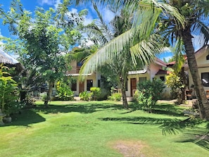 Un jardín tropical con palmeras, una construcción de techo de paja y un césped bien cuidado.