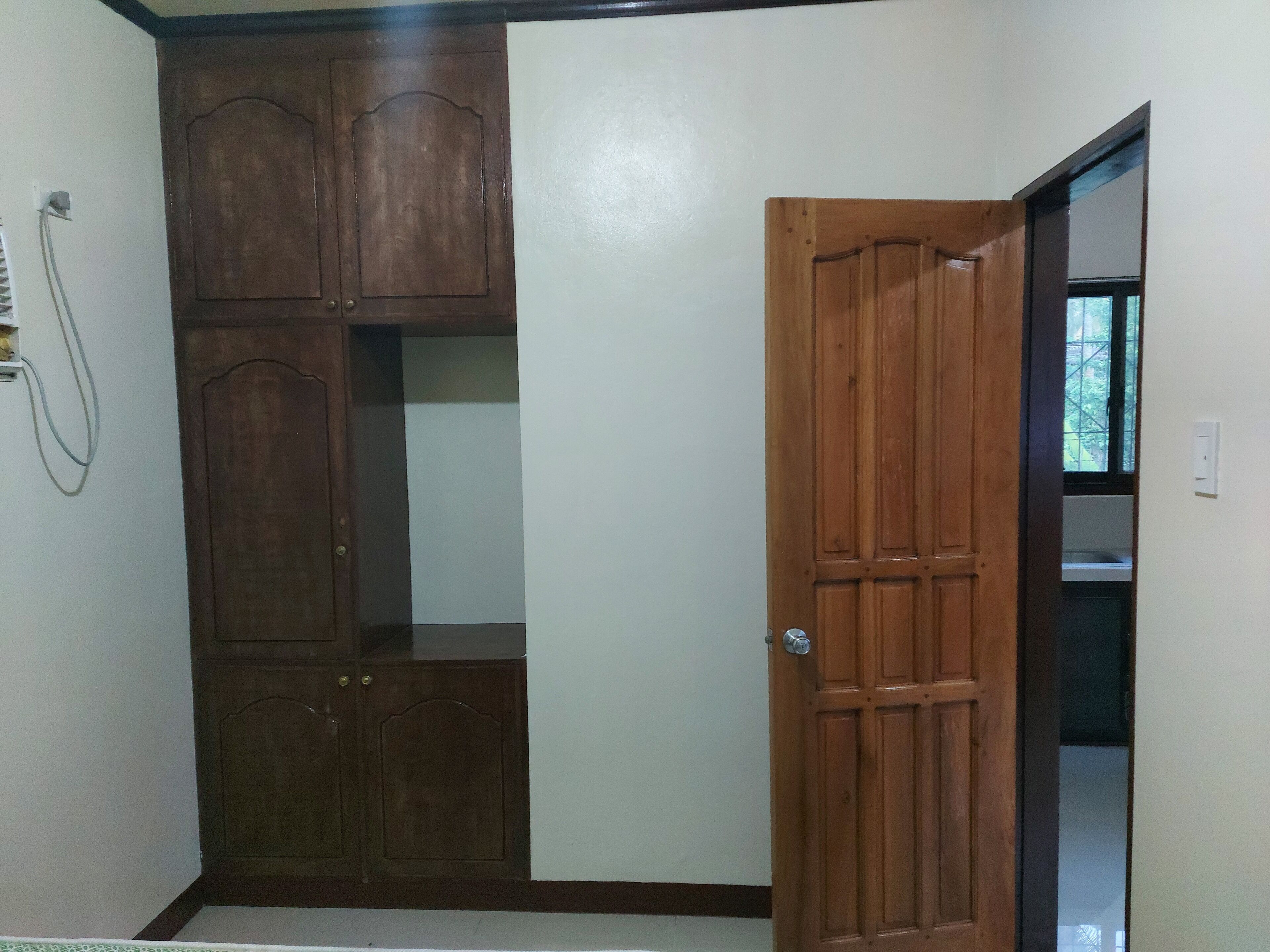 A room with a wooden wardrobe, a door, and a window.