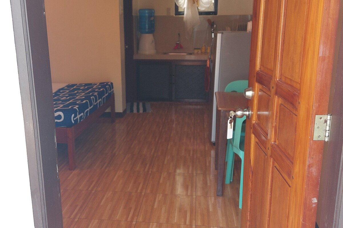 A compact kitchen with a sink, a clock on the wall, and a window with curtains.