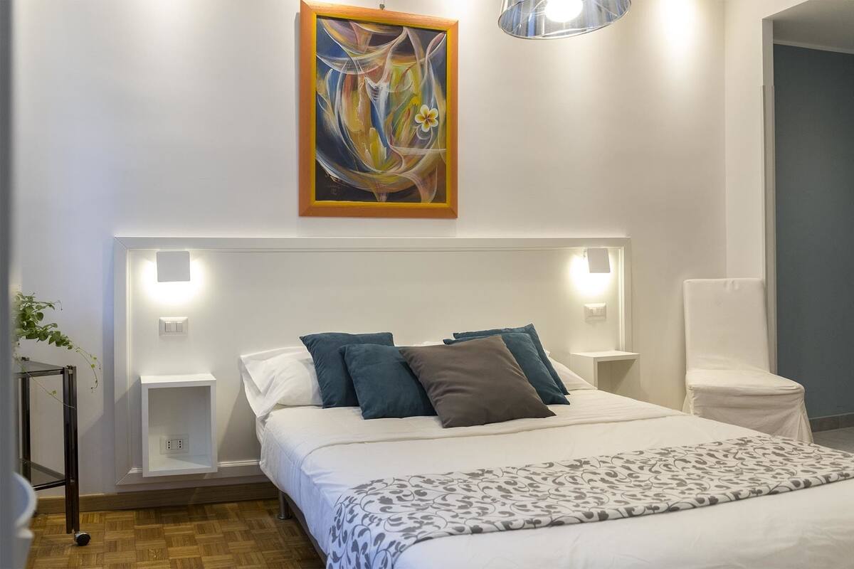 A modern bedroom with a large bed, bedside tables, a wall-mounted painting, and a bedside lamp.