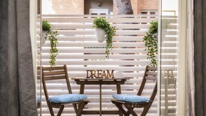 Dos sillas de madera con cojines azules y una mesa con la palabra "DREAM", frente a una cerca blanca de listones con plantas colgantes.