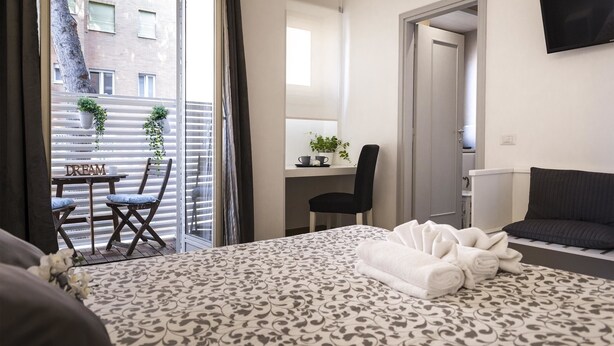 Una habitación de hotel con cama, escritorio, silla, televisor y balcón con plantas.