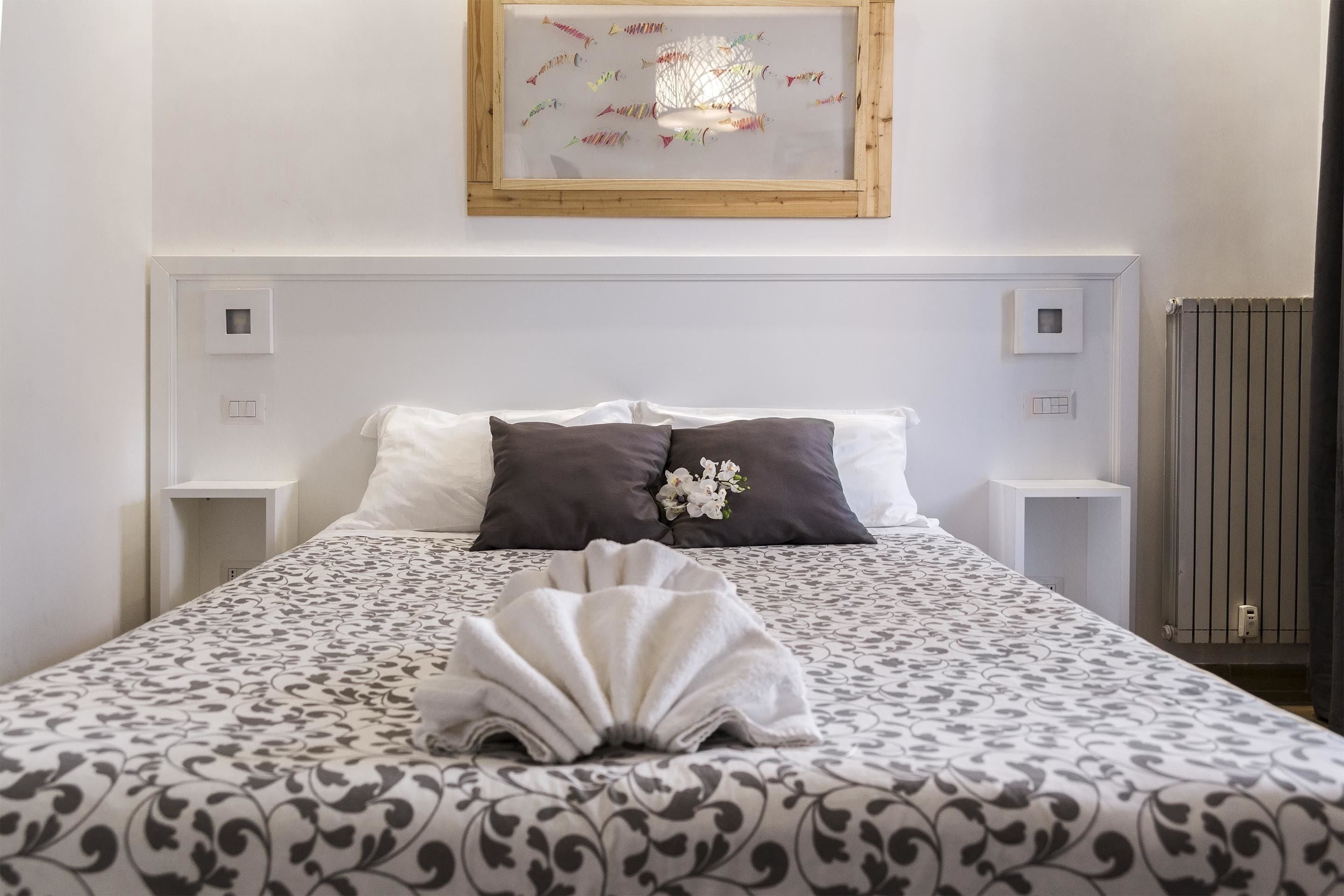 A neatly made bed with a patterned bedspread, two pillows, a decorative towel, and a framed artwork above.