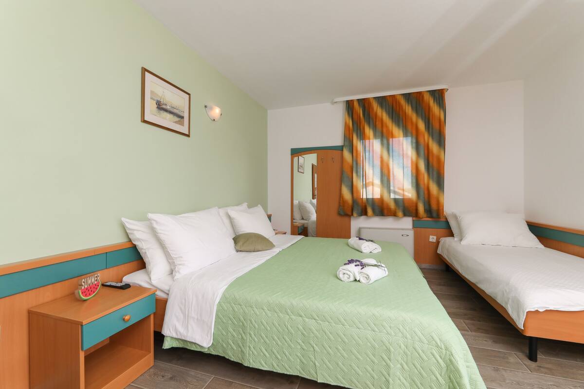 A hotel room with a bed, a nightstand, a mirror, and a window with curtains.
