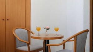 Une petite table ronde avec deux chaises, un vase avec une fleur et deux verres de jus d’orange.