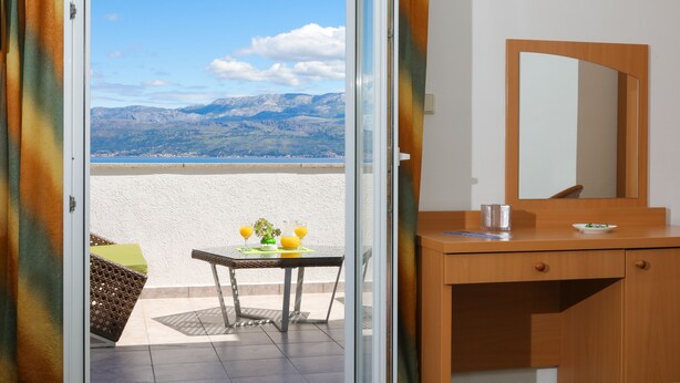 Une chambre avec vue sur les montagnes, une table avec deux verres de jus d’orange et un bureau en bois avec un miroir.