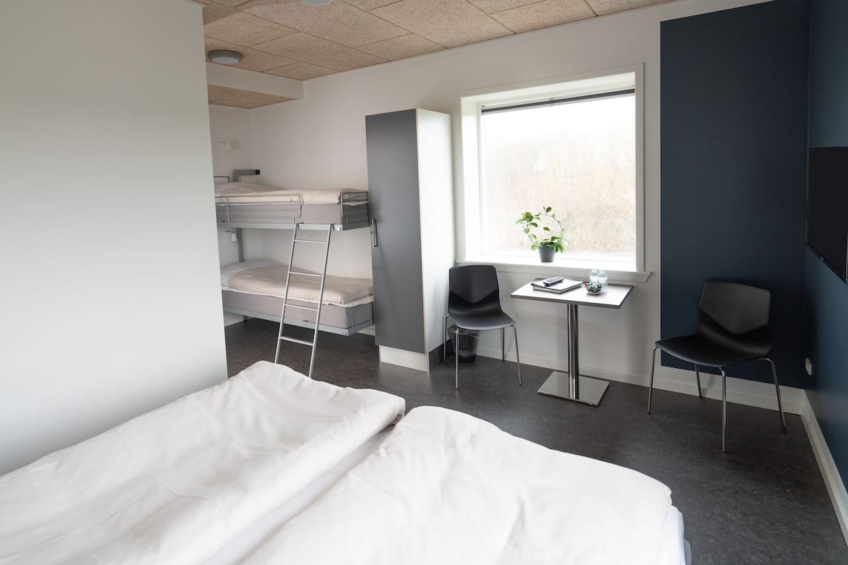 A modern hotel room with bunk beds, a desk with a chair, a small table, and a window with a view.