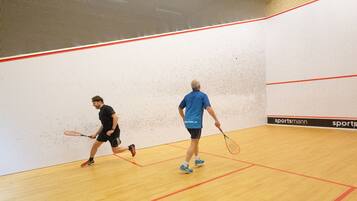 Dos personas jugando squash en una cancha interior con suelo de madera y líneas rojas que marcan los límites de la cancha.
