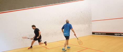 Two people playing squash in an indoor court with a wooden floor and red lines marking the court boundaries.