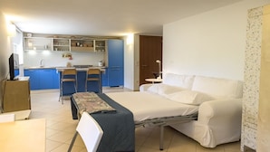 Pieni hotellihuone, jossa on sänky, pieni työpöytä, tuoli, pieni keittiönurkkaus ja kylpyhuone.