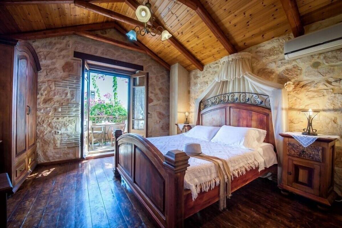 A bedroom with a wooden bed, stone walls, and a view of greenery outside.