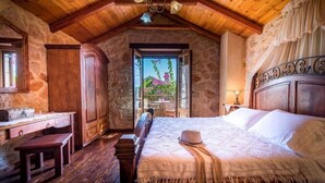A rustic bedroom with a wooden ceiling, a large bed, a desk, and a view of the outdoors. - Ktima Kourou (Zakynthos)
