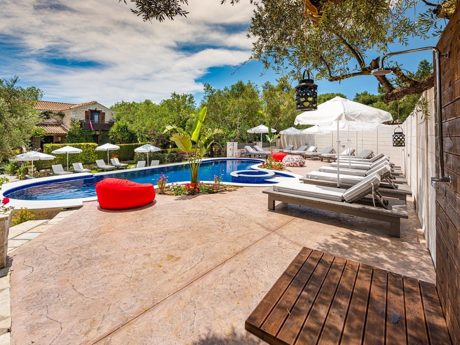 A pool area with lounge chairs, a red bean bag, and umbrellas.
