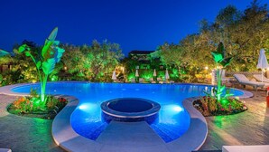 A swimming pool with a hot tub, surrounded by lounge chairs and illuminated plants. - Ktima Kourou (Zakynthos)
