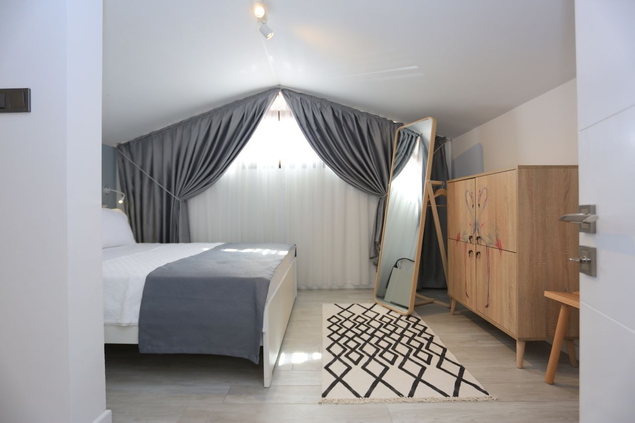 A bedroom with a bed, a wardrobe, a mirror, and a geometric rug.