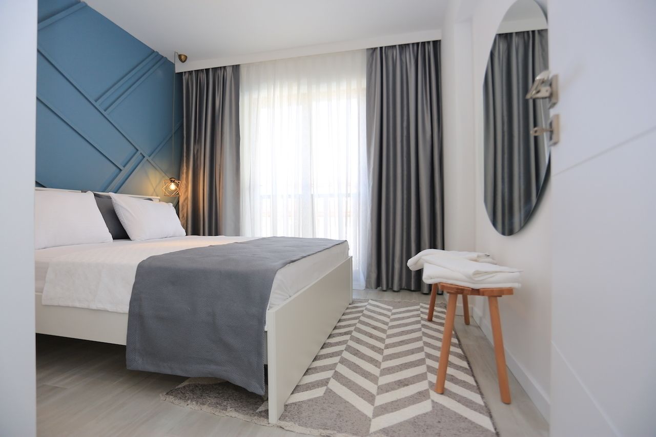 Un dormitorio moderno con cama, mesita de noche, espejo y ventana con cortinas.