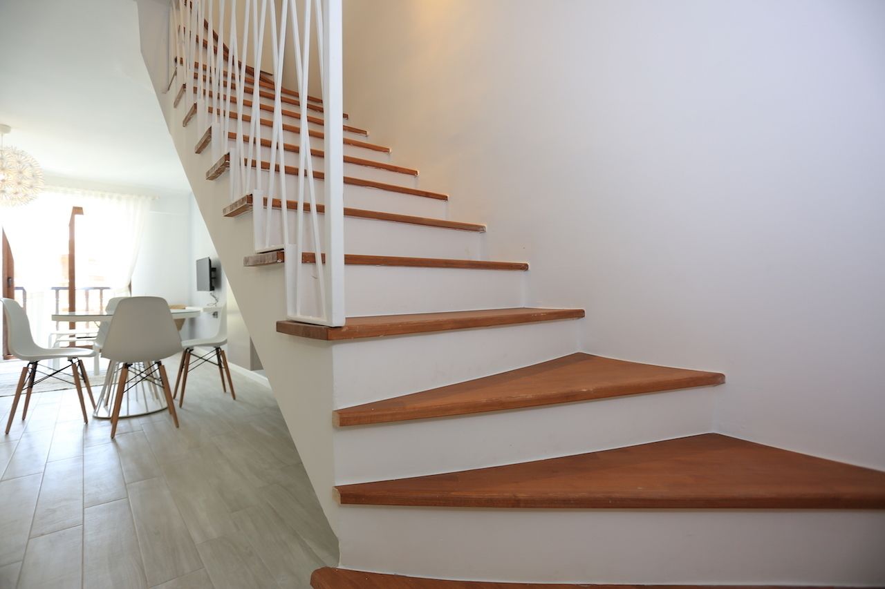 Una escalera moderna con escalones de madera y barandillas blancas, que conduce a un comedor con sillas y una mesa blancos.