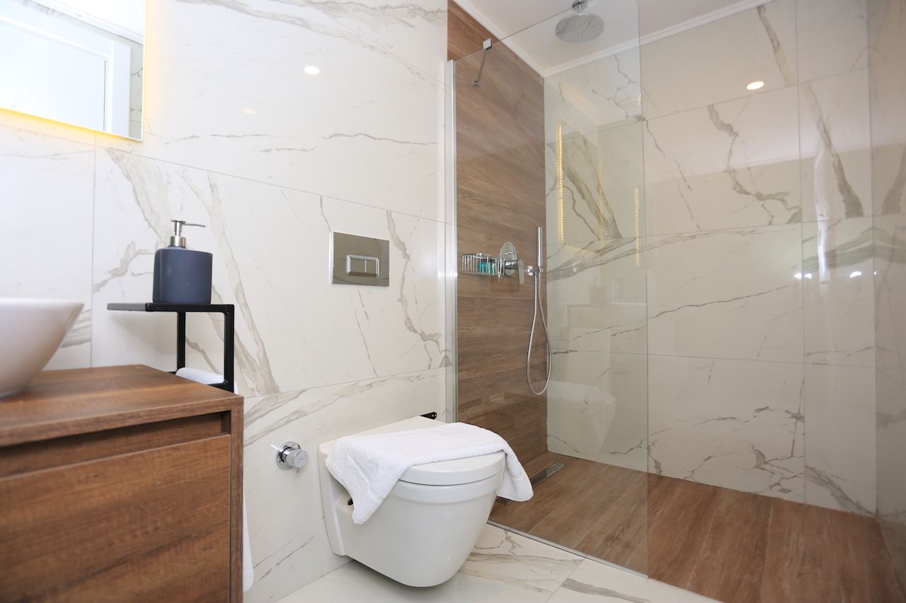 A modern bathroom with a marble floor, a glass shower enclosure, and a wooden vanity with a sink.