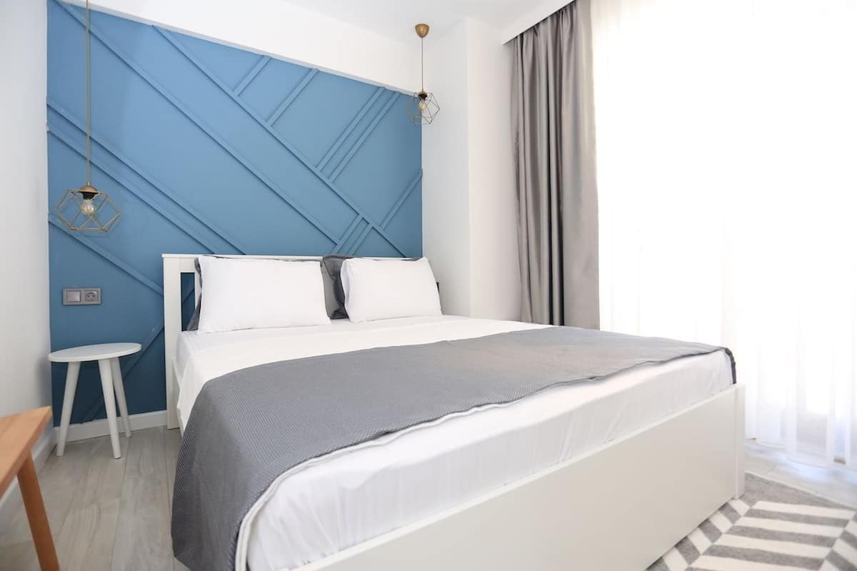 A modern bedroom with a large bed, a small side table, and a blue accent wall.