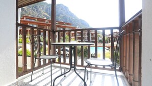 Un balcon avec deux tables et des chaises, donnant sur une piscine et des bâtiments situés dans une région montagneuse.