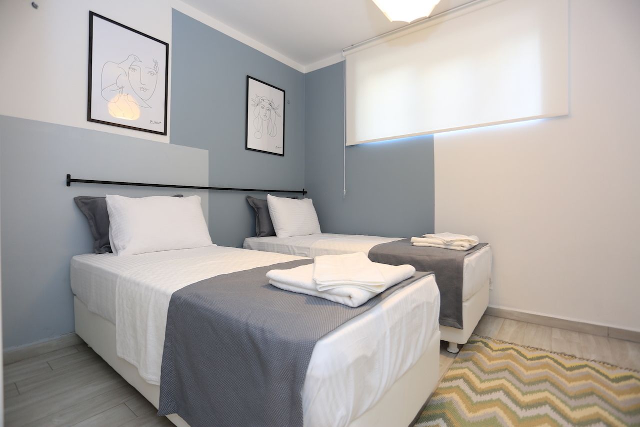Quarto de hotel com duas camas, uma mesa pequena e uma janela com persianas.