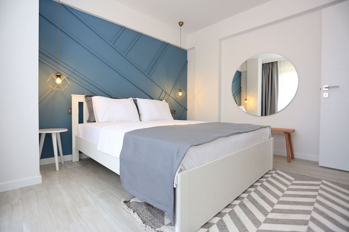 A modern bedroom with a bed, bedside table, and a round mirror on the wall.