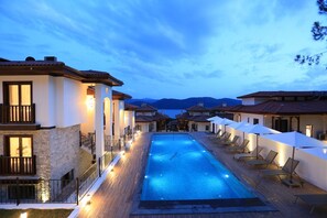A swimming pool with lounge chairs and umbrellas, surrounded by buildings with stone and tiled facades. - Verde Suites Akyaka (Ula)