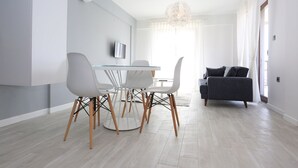 Un salon moderne comprenant un coin repas, un canapé gris et un téléviseur fixé au mur.