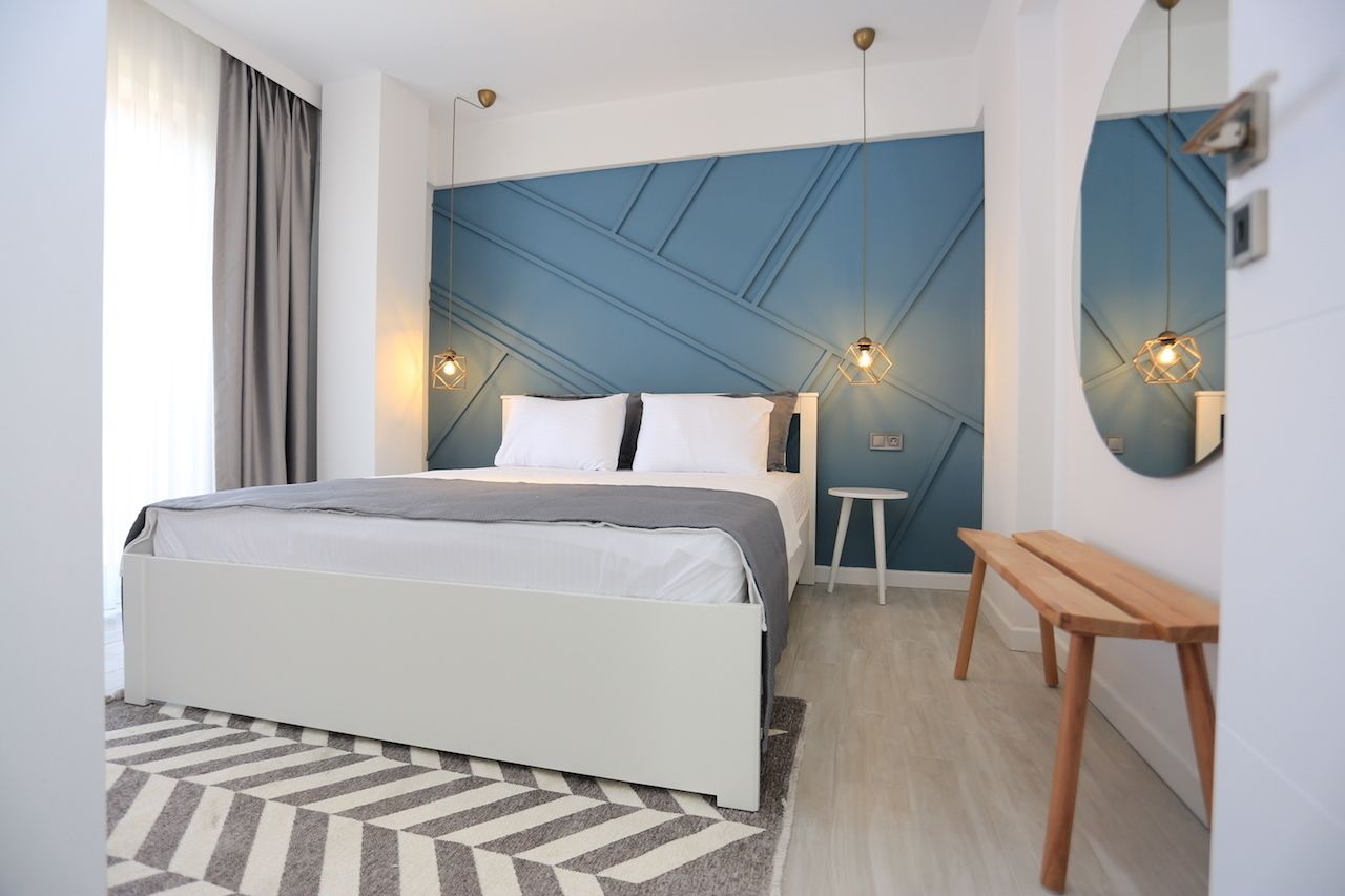 Un dormitorio moderno con una cama, mesitas de noche, un espejo y una alfombra con estampado geométrico.