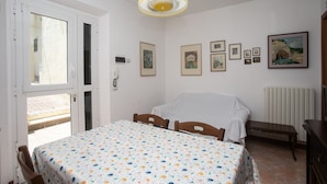 A room with a bed, a table with a patterned tablecloth, a bench, and a wall with framed pictures. - S202 - Sirolo, new two-room apartment convenient to services (Sirolo)