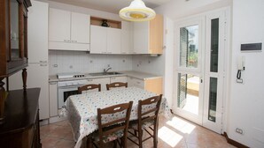 A kitchen with white cabinets, a dining table with chairs, a hanging light fixture, and a sliding glass door leading to an outdoor area. - S202 - Sirolo, new two-room apartment convenient to services (Sirolo)
