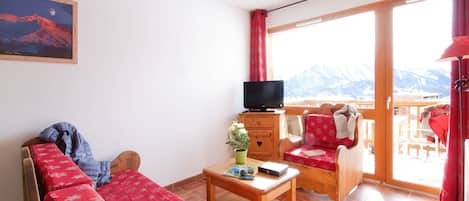 Una habitación acogedora con cama, televisión, mesa y vistas a montañas a través de amplios ventanales.