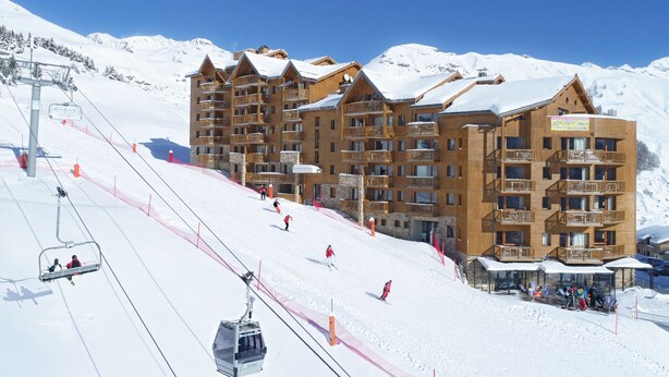 A ski resort with wooden buildings, ski lifts, and a snow-covered mountain backdrop.