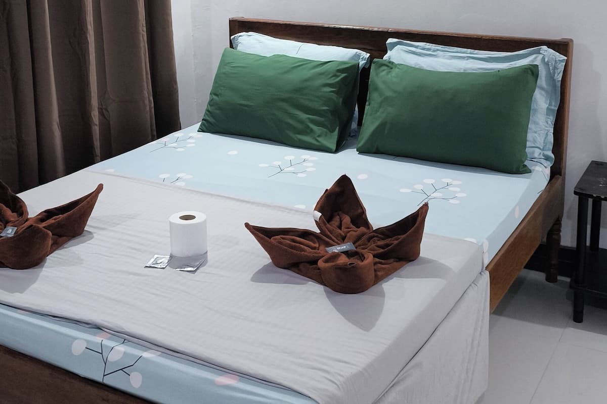 Un lit bien fait, orné de coussins verts, un tableau encadré accroché au mur et un rideau à la fenêtre.