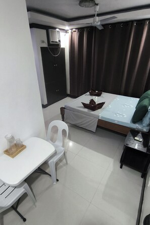 A compact hotel room with a bed, a small table, a chair, and a desk. - Jace's Travellers Inn (El Nido)