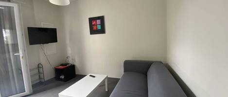 Una sala moderna con un sofá gris, una mesa de centro blanca, un televisor de pantalla plana montado en la pared y una mesita de noche con una lámpara.