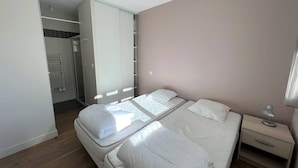 Un dormitorio con dos camas individuales, un armario, una mesita de noche con lámpara y un radiador.