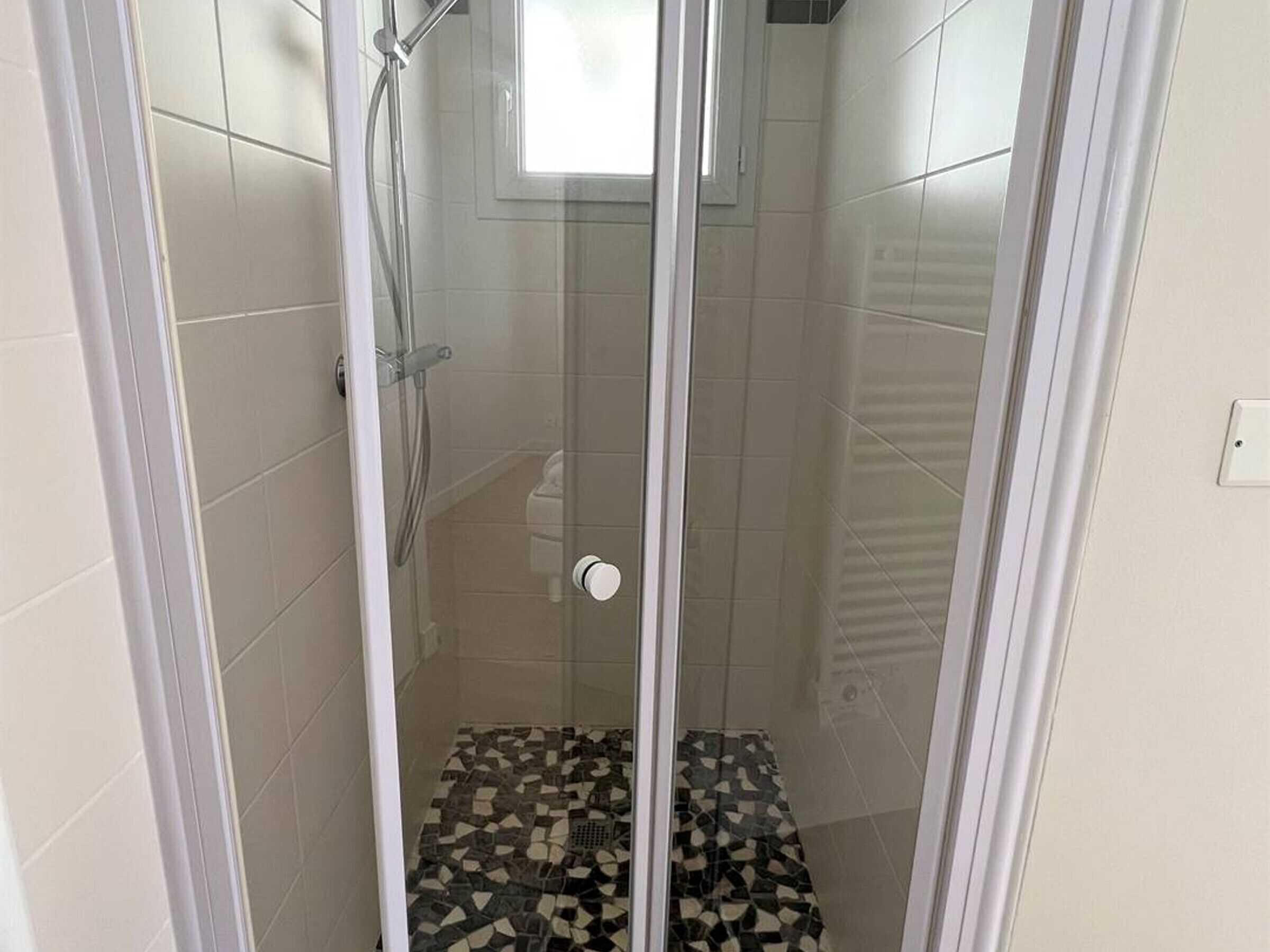 Un área de ducha con paredes de azulejos y suelo con diseño, protegida por un cerramiento de vidrio.