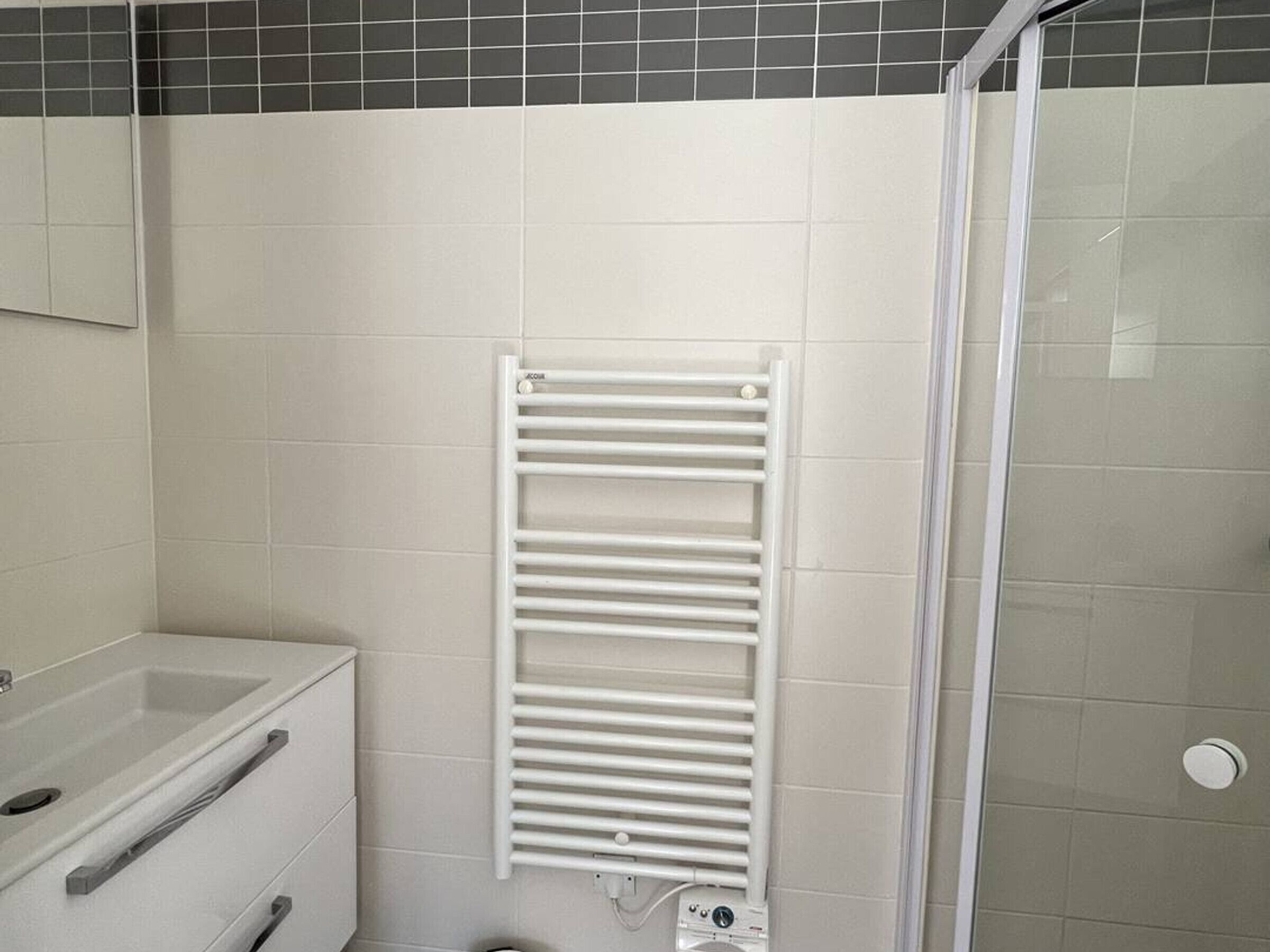 A bathroom with a white sink, a mirror, a towel rack, and a shower area.