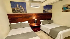A room with two beds, a wooden headboard, a nightstand with a lamp, and wall art depicting birds.