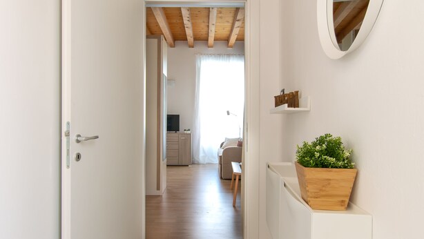 A hallway with a wooden ceiling, a white door, and a wooden planter with green plants. - Foresteria Della Corte (Como)